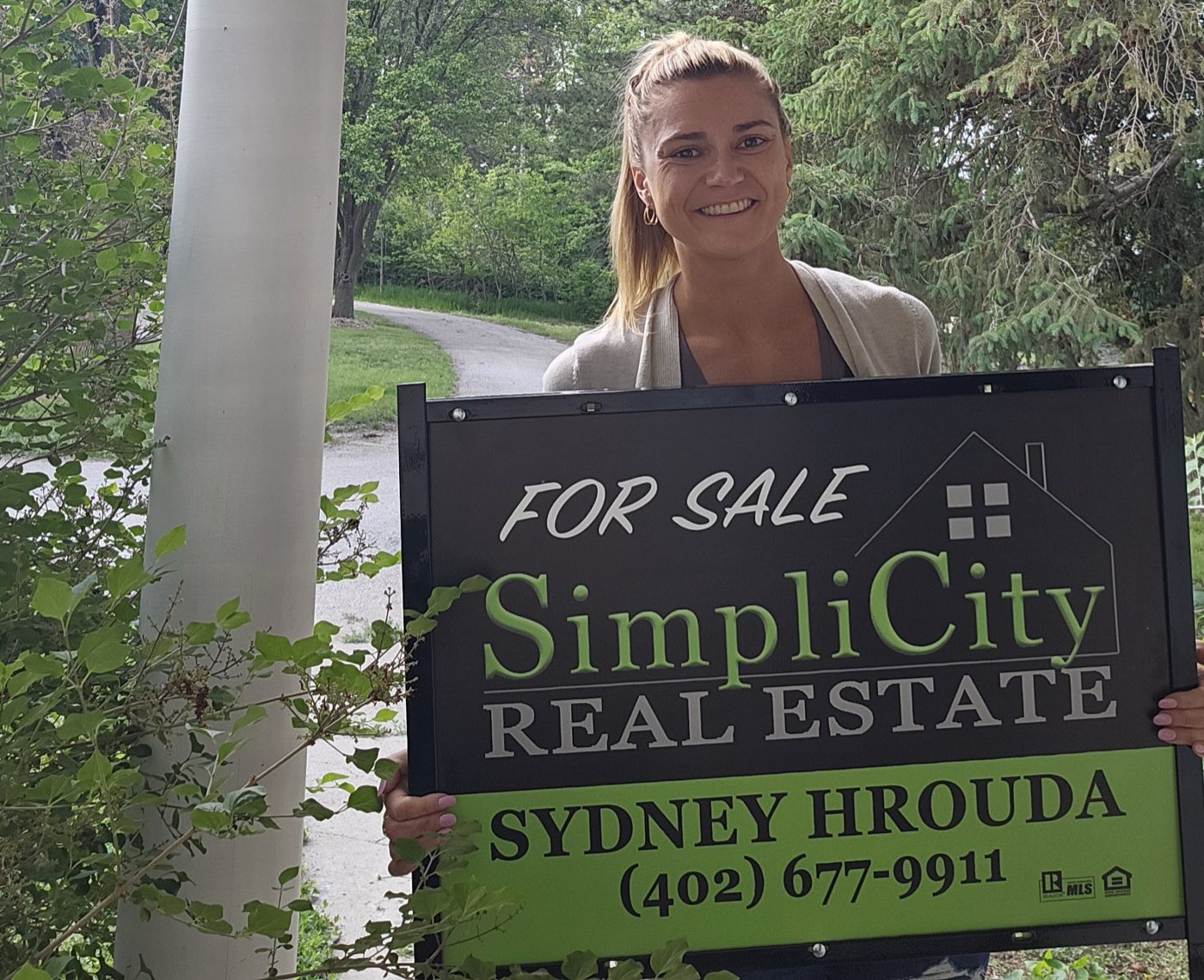 Sydney Hrouda with a SimpliCity Real Estate for sale sign east of Lincoln, Nebraska