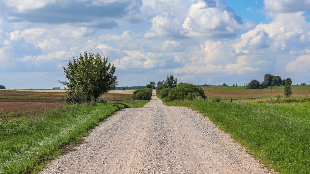 Scenic view of a gravel road through lush farmlands and fields under a blue sky in Poland.
