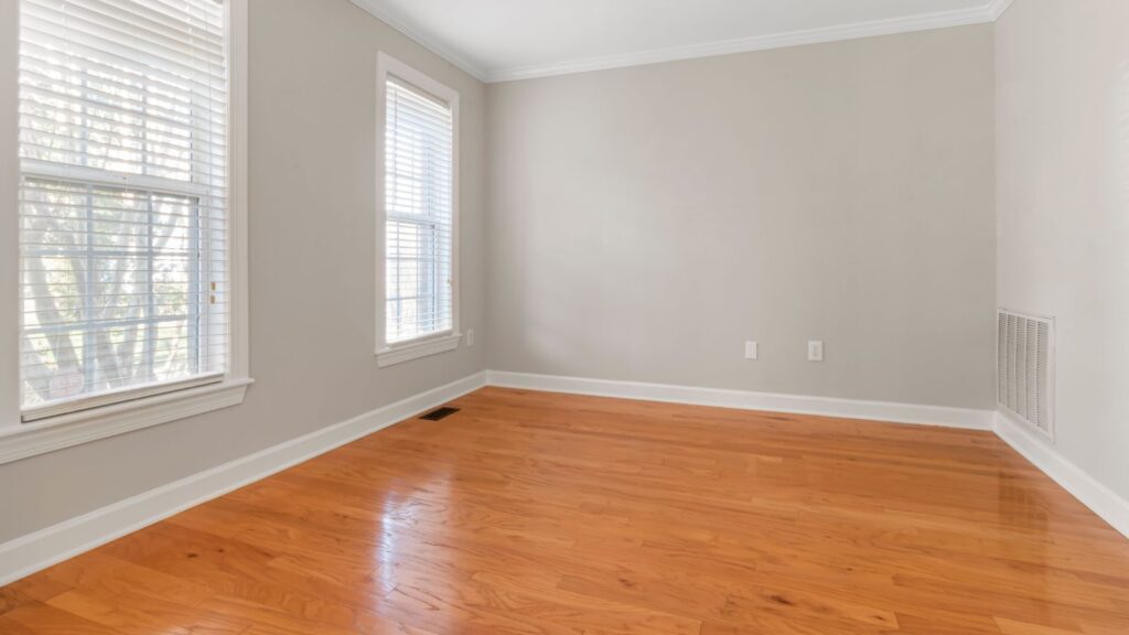 Spacious empty room with natural light, hardwood floors, and neutral walls.