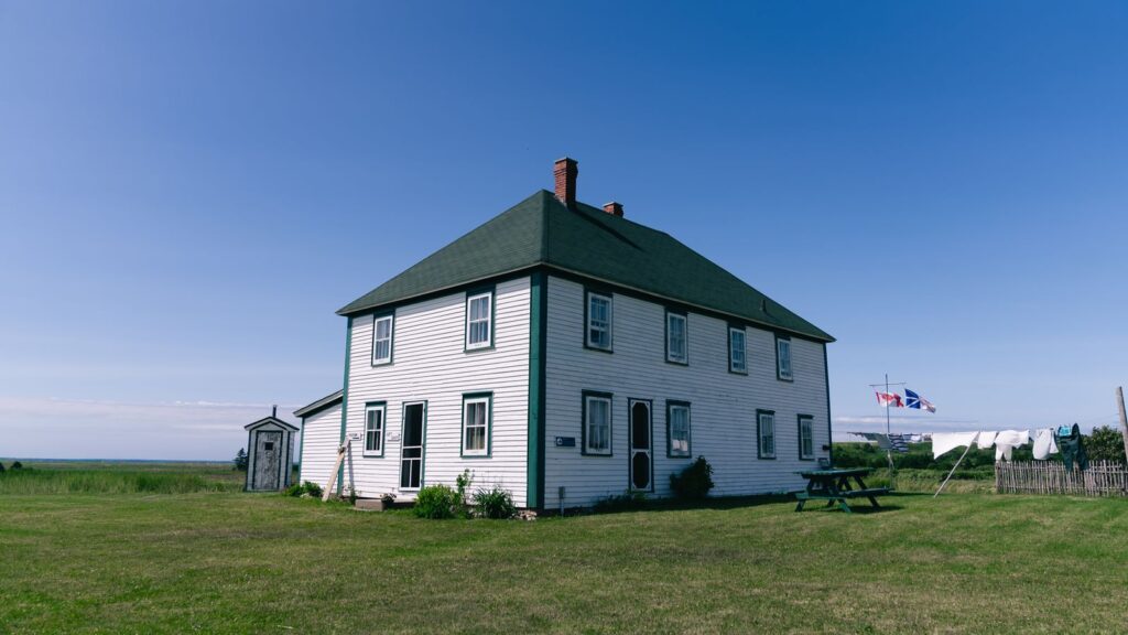 A scenic view of a white wooden house in a rural landscape under a clear blue sky.