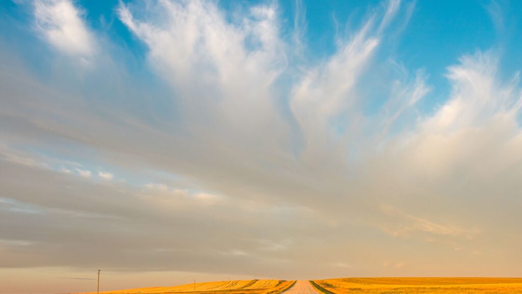 A vast prairie landscape in Saskatchewan with a rural road and dramatic clouds at sunset.