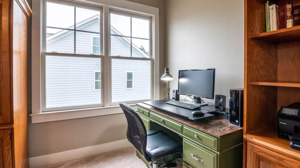 A neat and cozy home office setup with a desk, monitor, and window view.