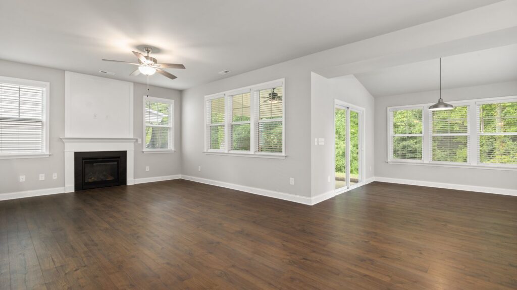 Contemporary empty living room with hardwood flooring, fireplace, and large windows.